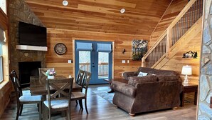 A cozy cabin interior with a stone fireplace, wooden walls, a dining area, a sofa, and a staircase. - Blue Jay Riverfront cozy cabin along the Nottley River in Murphy, North Carolina (Murphy)