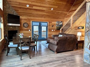 A cozy cabin interior with a stone fireplace, wooden walls, a dining area, a sofa, and a staircase. - Blue Jay Riverfront cozy cabin along the Nottley River in Murphy, North Carolina (Murphy)