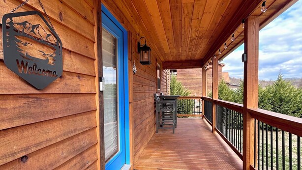 A wooden deck with a blue door, a welcome sign, and a view of the surrounding landscape. - Blue Jay Riverfront cozy cabin along the Nottley River in Murphy, North Carolina (Murphy)