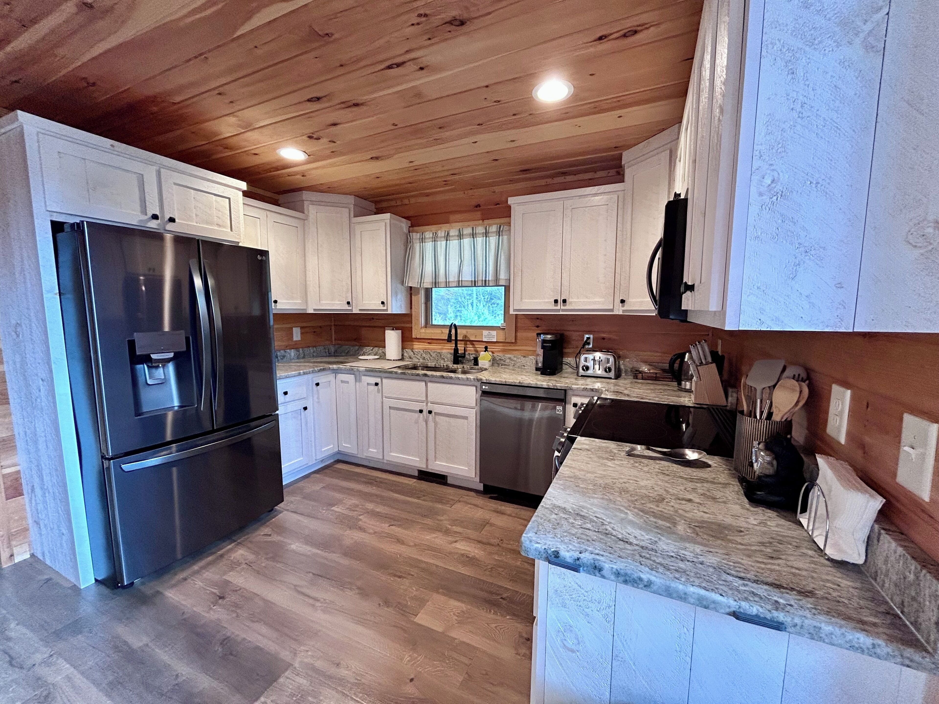 A modern kitchen with white cabinets, stainless steel appliances, and a wooden ceiling.