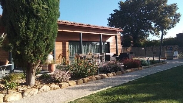 Et moderne hus med en patio, omgivet af en velplejet have med forskellige planter og græsplæne.