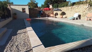 En swimmingpool med træterrasse, omgivet af småsten og en stenvæg.