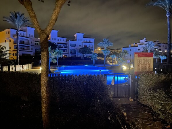 A nighttime view of a hotel with a swimming pool, palm trees, and illuminated buildings. - Lovely apartment in the beautiful Hacienda Riquelme Golf Resort (Sucina)