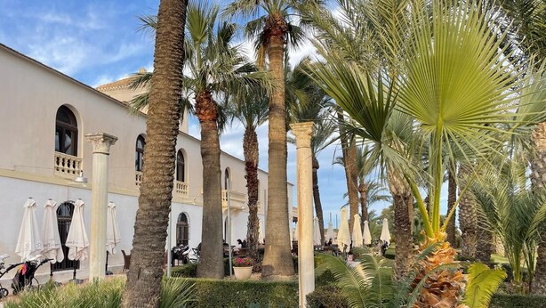 Une cour intérieure agrémentée de palmiers, un bâtiment orné d’arcades et des espaces de repos en plein air.