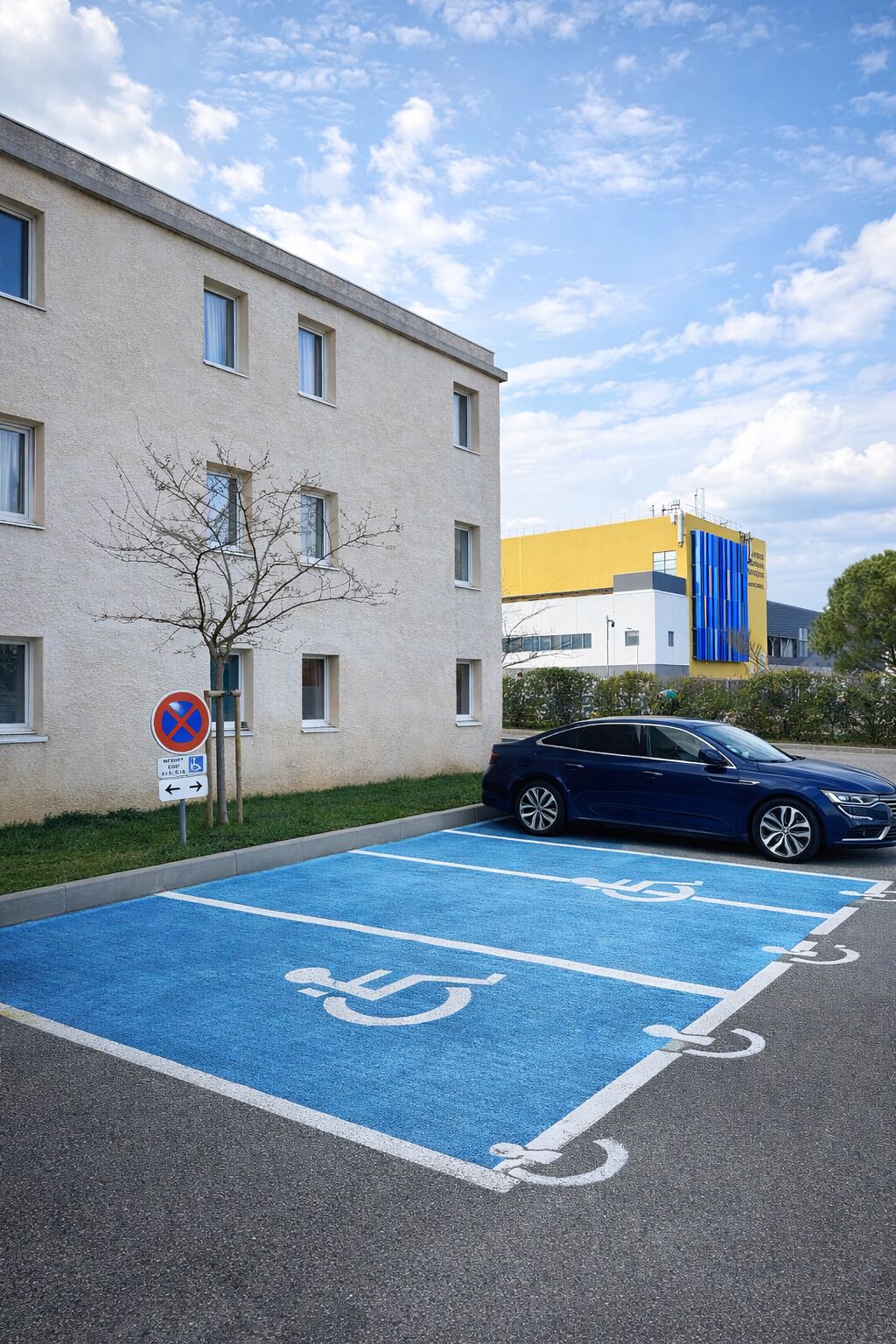 A parking area with blue handicapped parking spaces, a no parking sign, and a building with multiple windows.