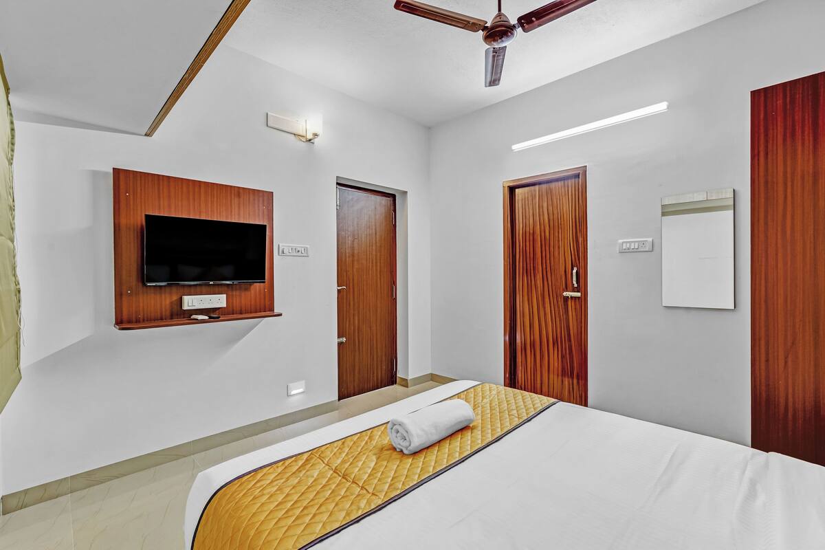 Ein Hotelzimmer mit einem Bett, einem an der Wand befestigten Fernseher, einem Deckenventilator und Holztüren.
