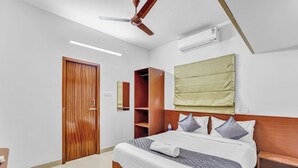 A hotel room with a wooden bed, a ceiling fan, an air conditioning unit, a wooden wardrobe, and a bedside table. - Ecostay Valasaravakkam (Chennai)