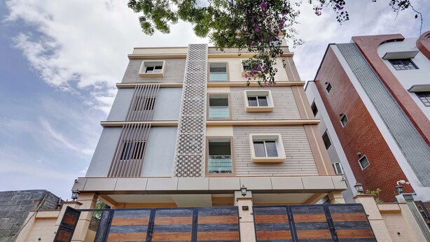 A multi-story residential building with a modern design, featuring a central vertical decorative panel, multiple windows, and a large garage door. - Ecostay Valasaravakkam (Chennai)