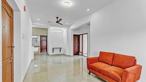 A spacious, well-lit hallway with a polished floor, a wooden door, and a modern orange sofa. - Ecostay Valasaravakkam (Chennai)