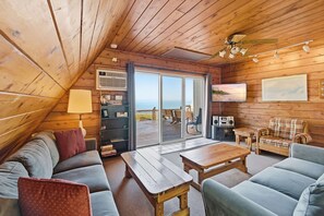 A cozy cabin interior with a wooden ceiling, a sofa, a table, and a television. - Juniper Presents Chalet #17: Lake Views & Resort Amenities (Stevensville)