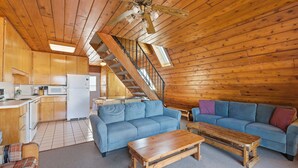 A log cabin interior with a kitchen, two blue sofas, a wooden coffee table, and a staircase. - Juniper Presents: Chalet #17 w Lake Views & Resort Amenities (Stevensville)