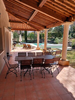 Une terrasse extérieure dotée d’une pergola en bois, d’un sol carrelé et offrant une vue sur la piscine.