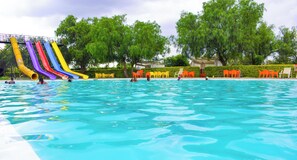 Ein Schwimmbecken mit mehreren Wasserrutschen und Außenbereich mit Sitzgelegenheiten.