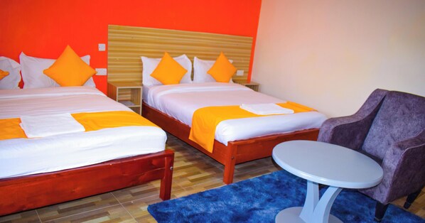 Zwei Betten mit orangefarbener Bettwäsche, ein kleiner runder Tisch und ein violetter Sessel in einem Zimmer mit Holzböden.