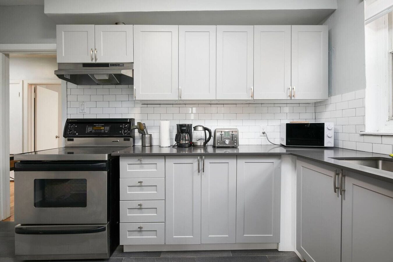 A modern kitchen with white cabinets, a stainless steel stove, a microwave, and a coffee maker.