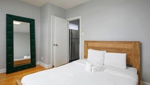 A bedroom with a bed, a mirror, a door, and a refrigerator.