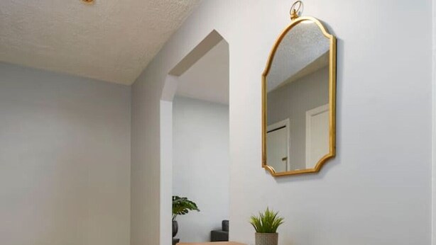 A hallway with wooden flooring, a wooden console table, a mirror, and a ceiling light.