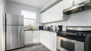 A modern kitchen with stainless steel appliances, white cabinetry, and a tiled backsplash.