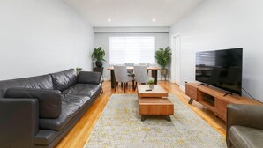 A modern living room with a leather sofa, a wooden coffee table, a TV on a wooden stand, and a dining area with chairs and a table.