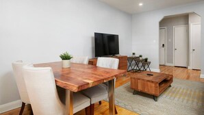 Ein modernes Wohnzimmer mit Esstisch aus Holz, einem Fernseher und einem kleinen Beistelltisch mit Pflanzen.