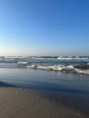 En strand med bølger, der slår ind mod kysten under en klar himmel.