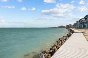 Une promenade en bord de mer avec une terrasse en bois, une côte rocheuse et des bâtiments en arrière-plan.
