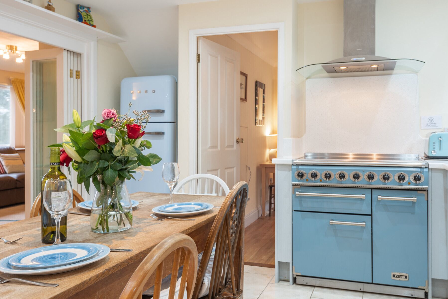 A kitchen with a blue stove, a refrigerator, and a dining table set with plates and a vase of flowers.
