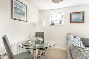 A dining area with a glass table, chairs, and a window with blinds. - Zephyr - One Bedroom Apartment, Sleeps 2 (Fowey)