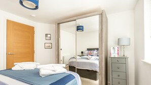 Quarto com cama, guarda-roupa, espelho e mesa de cabeceira com abajur.