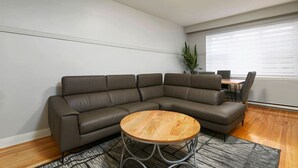 Ein modernes Wohnzimmer mit einer Eckcouch, einem runden Holztisch und einem Essbereich mit Tisch und Stühlen.