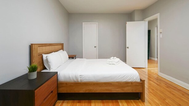 Ein Schlafzimmer mit einem hölzernen Bett, weißer Bettwäsche, einem Nachttisch mit Pflanze und einem Kleiderschrank.