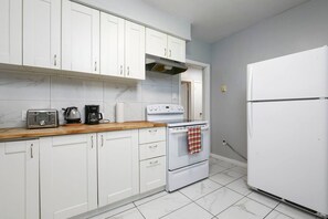 Une cuisine avec des meubles blancs, une cuisinière, un grille-pain et un réfrigérateur.