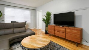 Ein modernes Wohnzimmer mit einer Ledersofa, einem Holztisch, einem Fernseher auf einer Holzkommode und einer Topfpflanze.