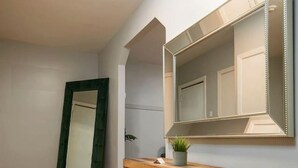 Ein modernes Badezimmer mit Holzboden, einem Holz-Konsolentisch, einem großen Spiegel und einer Deckenleuchte.