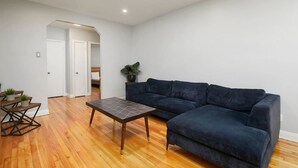 Ein modernes Wohnzimmer mit einem dunkelblauen Ecksofa, einem Holztisch und einem kleinen Beistelltisch mit Pflanzen.