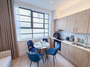 A compact kitchen with a dining area, featuring a round table, four chairs, and modern appliances. - Chic studio flat in Regent's Park near Marylebone (London)