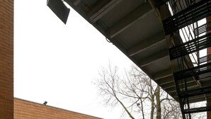 Ett vått betonggolv med ett metallräcke och en byggnad i tegel som syns i bakgrunden.
