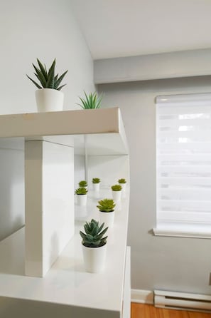 Una habitación moderna con una consola blanca, una planta en maceta y una ventana con persianas.