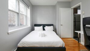 Een kleine, moderne hotelkamer met een enkel bed, een nachtkastje, een stoel en een kledingkast.
