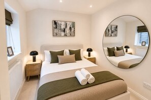 A hotel room with a large bed, two bedside tables with lamps, a round mirror, and artwork on the walls.