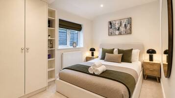A bedroom with a bed, bedside tables, a wardrobe, a window with blinds, and a painting on the wall.