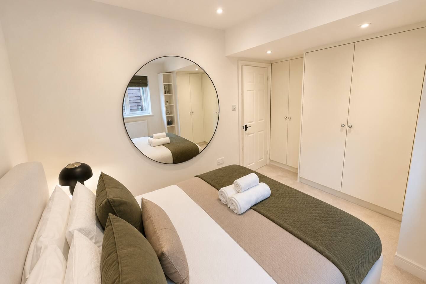 A bedroom with a bed, a round mirror, a wardrobe, and a nightstand.