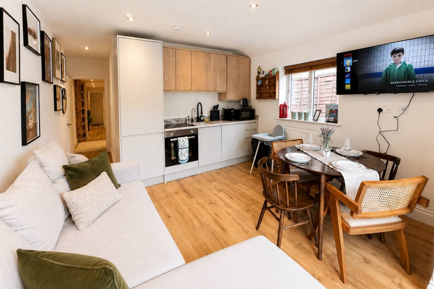 A modern living space with a sofa, dining table, chairs, a kitchen area, and a television.