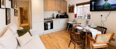 A modern living space with a sofa, dining table, chairs, a kitchen area, and a television.