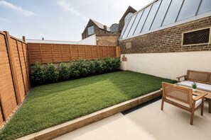 A backyard with a wooden fence, a grassy lawn, a brick wall, and a wooden bench.