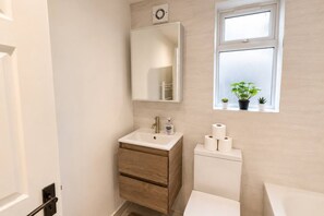 A bathroom with a sink, mirror, toilet, and a window with plants.