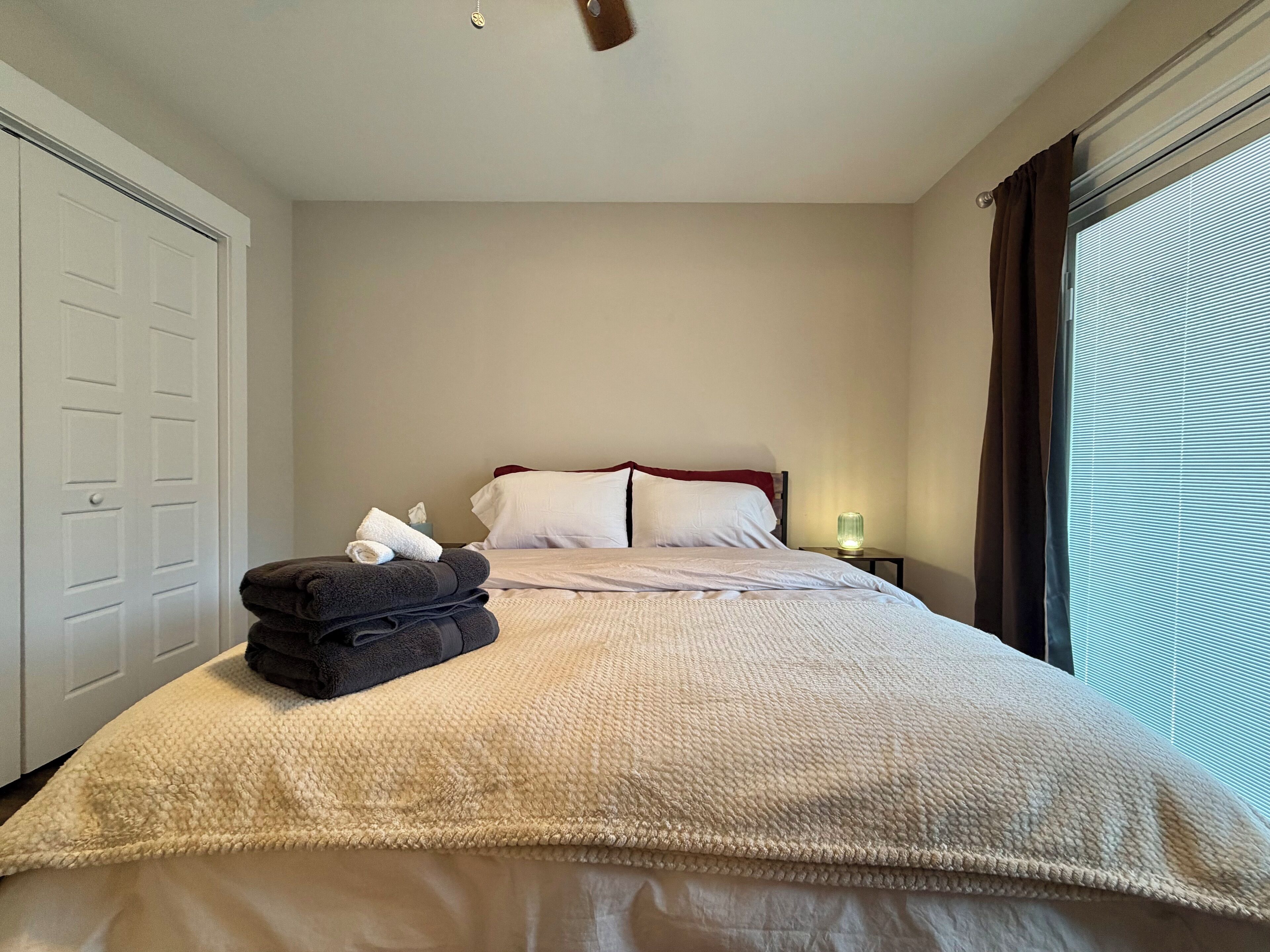 A neatly made bed with a beige blanket, a pillow, and a folded towel on the side.