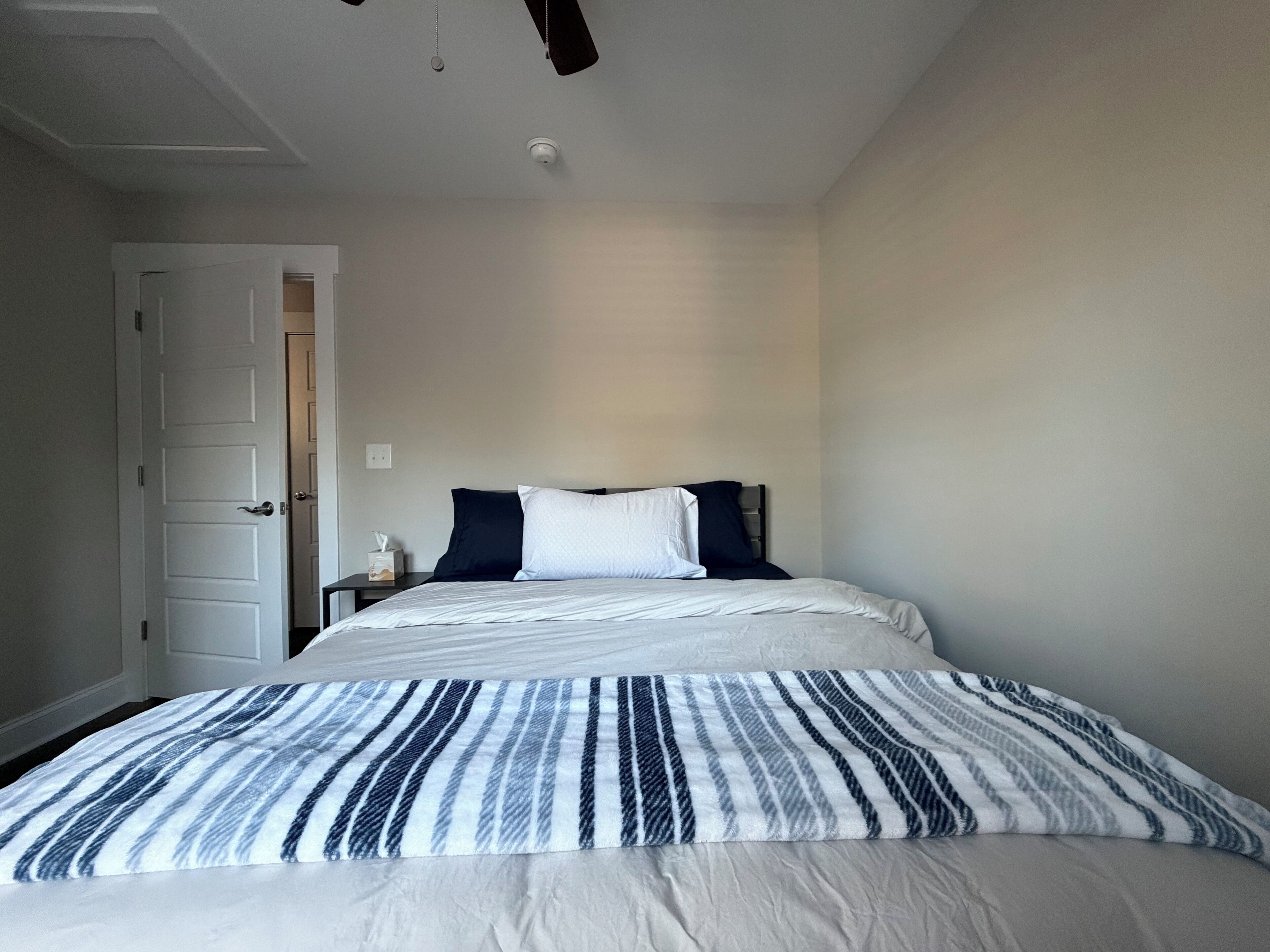 A bedroom with a bed, a nightstand, a door, and a ceiling fan.