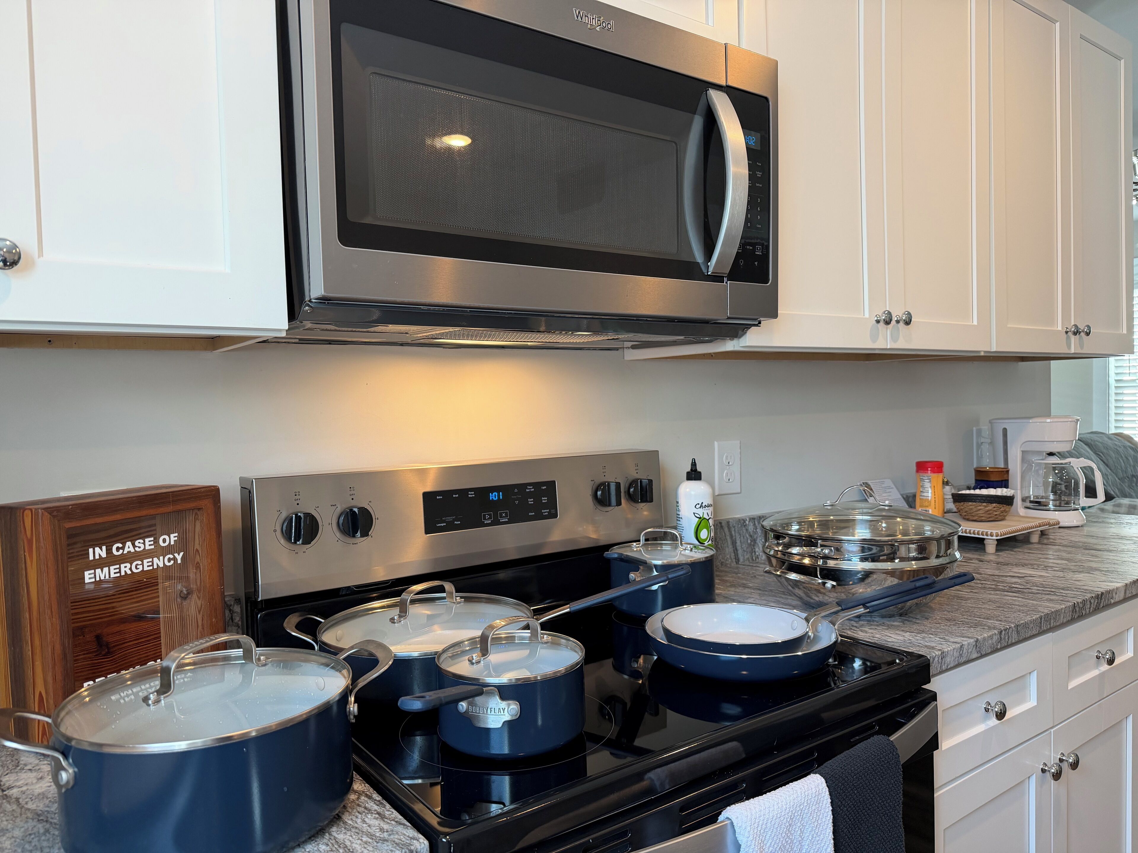 A kitchen with stainless steel appliances, including a microwave and stove, and a sign that reads "IN CASE OF EMERGENCY".