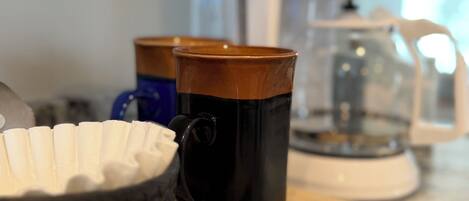 Un comptoir de cuisine avec une machine à café, un bol et deux tasses.